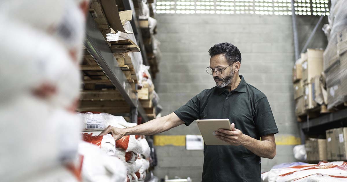 Individual in warehouse checking inventory with a tablet